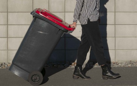 A woman putting a wheelie bin out.