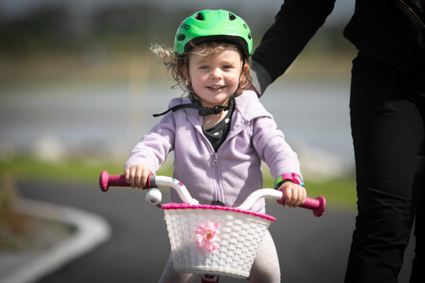 Pre-school aged child on their bicycle with a front basket being supported by an adult.